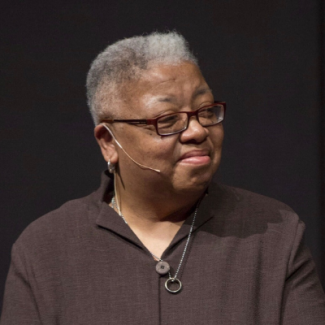 Gloria, wearing a microphone and brown shirt on, looking to the right