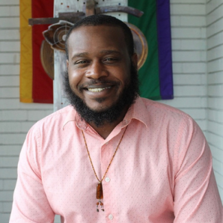 Jerron smiling wearing a necklace and pink-printed shirt
