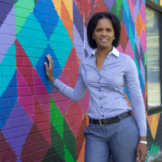 Latisha Johnson smiling against a colorful wall with a blue button-up shirt