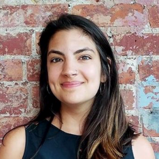 Margo Dalal smiling in a black shirt against a brick background